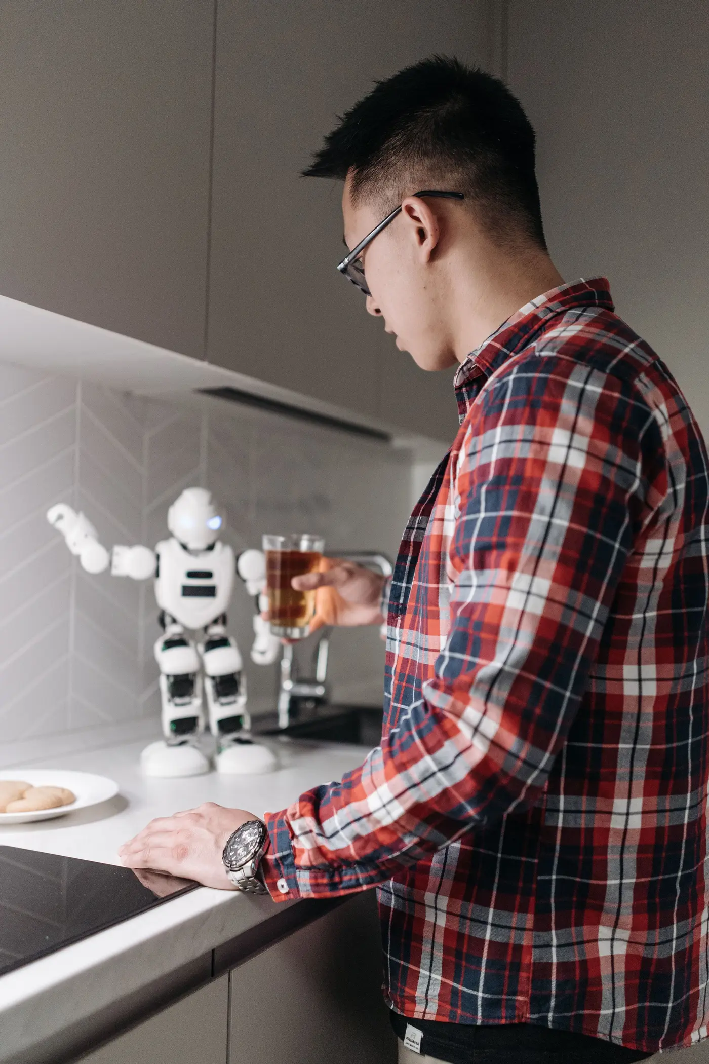 A man in a kitchen with a small humanoid robot standing on the counter