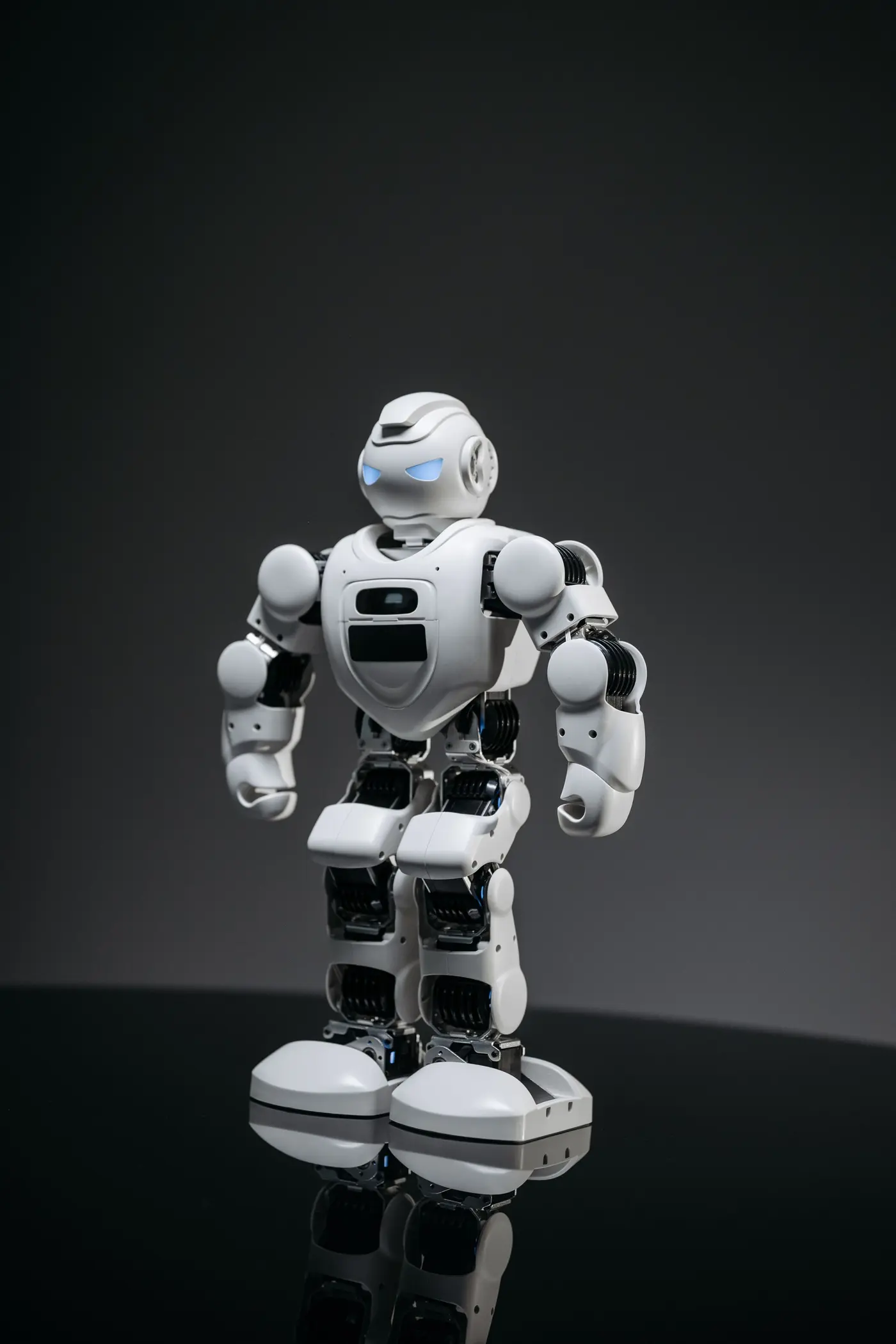 A small white humanoid robot lit against a black background