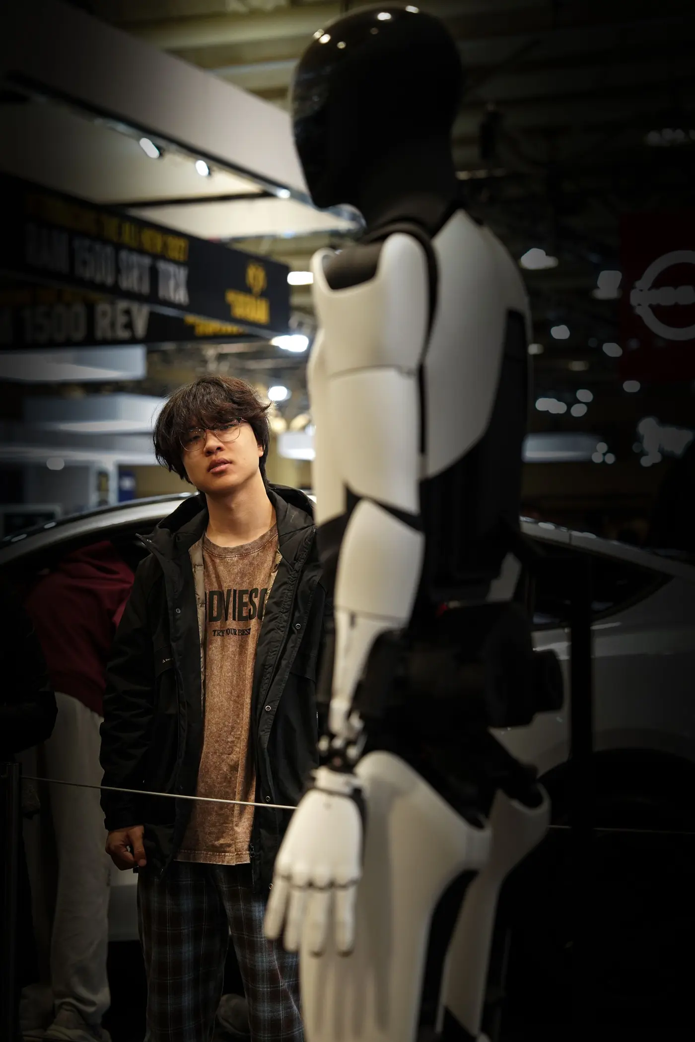 A young man sizing up a full-size humanoid robot on a shop floor