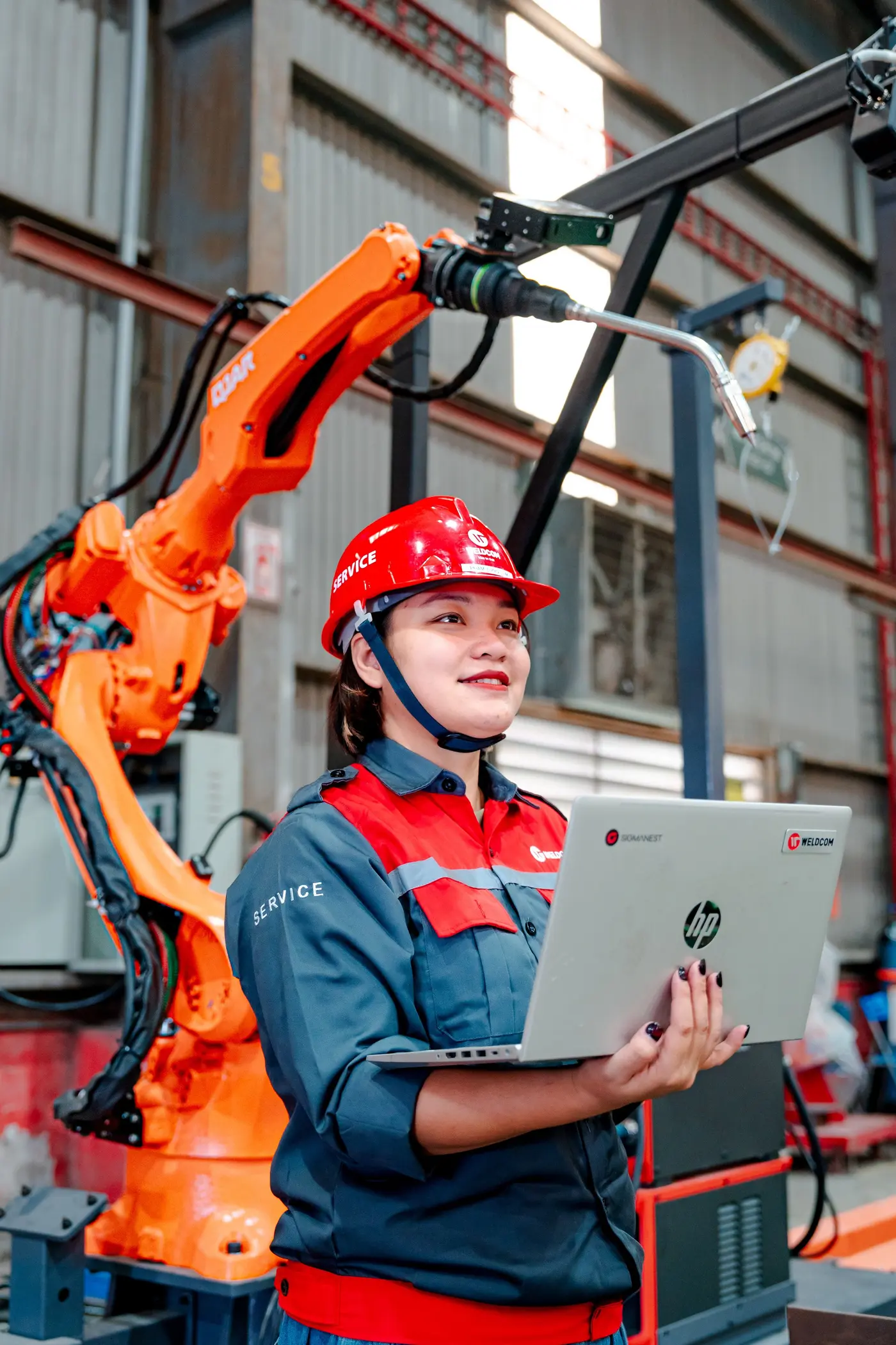 An engineer with a laptop overseeing a robotic arm in a factory